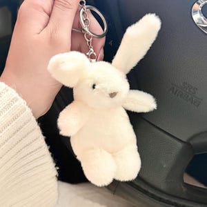 May include: White plush bunny keychain with a silver key ring. The bunny has a small, white nose and black eyes.