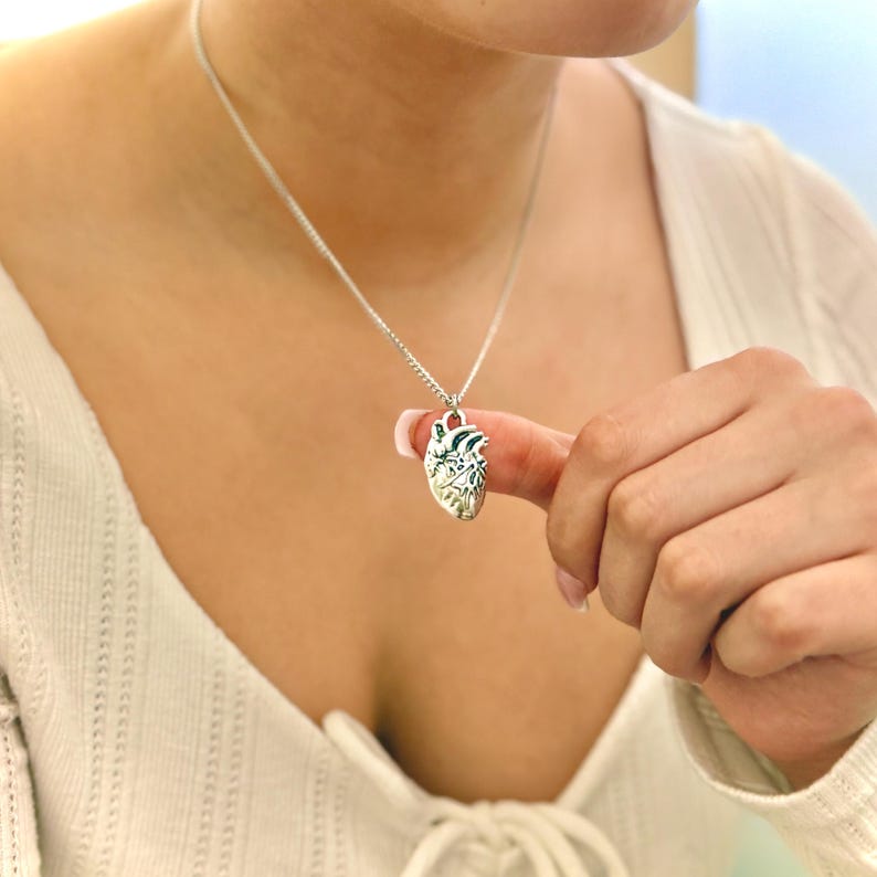 May include: A silver necklace with a detailed anatomical heart pendant.