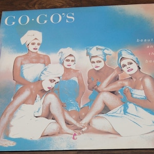 May include: A vintage vinyl record album cover featuring the band Go-Go's. The cover art shows five women wearing white towels and facial masks, with the album title "Go-Go's" in large, bold letters at the top and the text "beauty and the beat" in smaller letters at the bottom right.