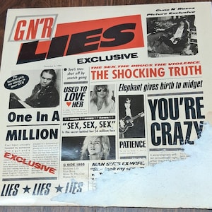 May include: A Guns N' Roses "Lies" album cover with the band's logo and the word "LIES" in large letters. The cover features various images and text, including the phrases "One In A Million" and "You're Crazy."