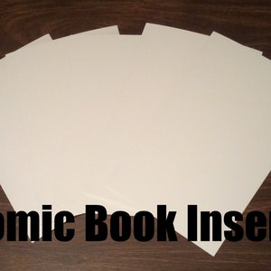 May include: A stack of white comic book inserts, arranged in a fan shape on a brown wooden surface. The text "Comic Book Inserts" is printed in black below the stack.