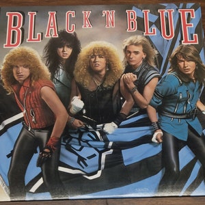 May include: Album cover for the band Black 'N Blue. The album cover features five people with long, curly hair, wearing leather and denim outfits. The band members are posed in front of a blue and black flag. The band's name is in red and white text.