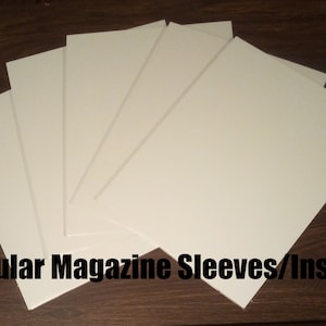 May include: Five white magazine sleeves or inserts on a wooden surface.