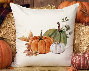 May include: A white throw pillow with a watercolor design of pumpkins and fall foliage. The pillow features three pumpkins: one orange, one green, and one white. The pumpkins are surrounded by leaves and branches in shades of brown, orange, and green.
