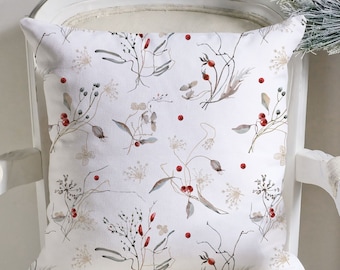Può includere: Cuscino quadrato decorativo con sfondo bianco e motivo botanico. Il design presenta illustrazioni dettagliate di rami, foglie e bacche rosse. Il cuscino è posto su una sedia bianca, suggerendo un'atmosfera di arredamento domestico accogliente.