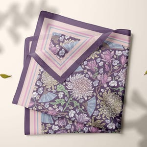 May include: A folded square scarf with a floral pattern in shades of purple, pink, and green. The design includes chrysanthemums, fans, and other floral elements. The scarf has a purple border with a light pink and blue inner border.