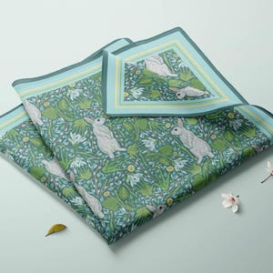 May include: A folded green and blue fabric with a white rabbit and floral pattern. The fabric has a yellow border.