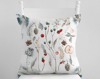 May include: A decorative throw pillow with a watercolor botanical design. The pillow features illustrations of berries, pinecones, leaves, and other natural elements in shades of red, brown, and blue on a white background. The pillow is displayed on a white chair.