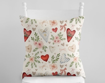 May include: A white cushion with a red, blue and white heart pattern. The hearts are surrounded by green leaves and pink flowers. The cushion is sitting on a white chair.