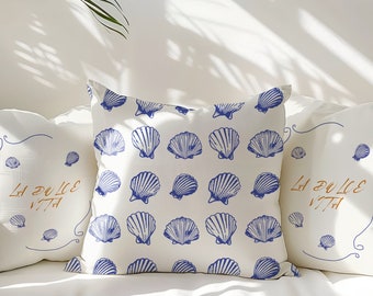 May include: Three white throw pillows with blue seashell patterns. The center pillow has a repeating pattern of blue seashells. The pillows on either side have the text "La Dolce Vita" in orange script.