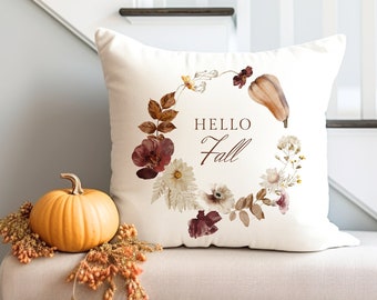 May include: A white throw pillow with a floral wreath design featuring dried leaves, flowers, and a small gourd. The wreath surrounds the text "HELLO Fall".