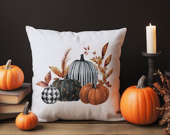 May include: White square pillow with a watercolor design of pumpkins in shades of orange, green, and black, with fall foliage. The pillow is on a wooden surface with orange pumpkins and lit candles.