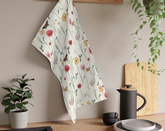 May include: A white kitchen towel with a floral pattern featuring butterflies, red, yellow, and pink flowers, and green leaves.