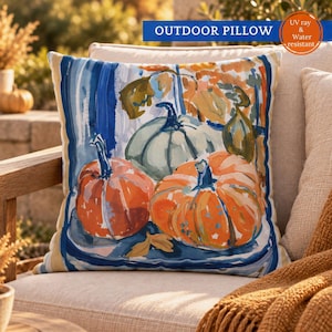 May include: A square outdoor pillow featuring a painterly illustration of orange and pale green pumpkins. The design includes bold blue brushstrokes and autumn foliage accents. The text OUTDOOR PILLOW and UV ray & Water resistant is visible.