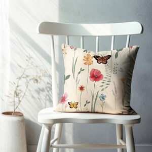 May include: A white chair with a cream-colored pillow featuring a floral pattern with butterflies. The pillow has a watercolor-like design with pink, red, yellow, and blue flowers.