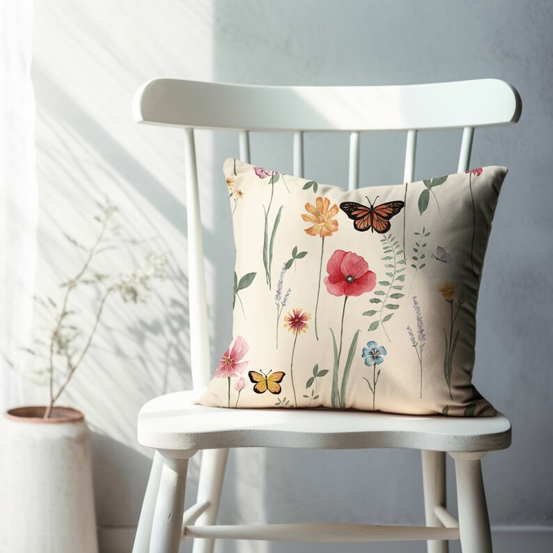 May include: A white chair with a cream-colored pillow featuring a floral pattern with butterflies. The pillow has a watercolor-like design with pink, red, yellow, and blue flowers.