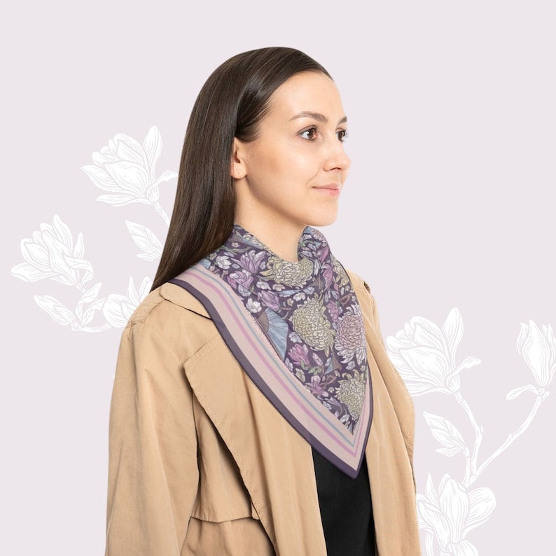 May include: A square scarf with a floral pattern in shades of purple, green, and pink. The scarf has a border with stripes of purple and pink. The scarf is worn around the neck.