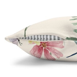 May include: A cream-colored pillow with a zipper closure features a watercolor floral design with pink, yellow, and blue flowers and butterflies.