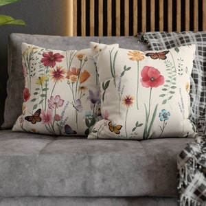 May include: Two decorative throw pillows with a floral pattern featuring butterflies, flowers, and leaves on a white background.