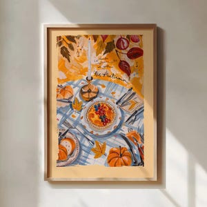May include: A framed art print featuring an autumn table setting with a blue and white checkered tablecloth, a berry tart, a tall candle, pumpkins, and cutlery. The text reads 'La-de-da, the leaves will fall, we gather, 'tis Autumn!' with musical notes.
