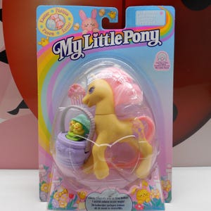 May include: A My Little Pony toy in its original packaging. The pony is yellow with a pink mane and tail. The packaging features a rainbow, Easter-themed graphics, and the text "My Little Pony". Includes a basket with chicks.