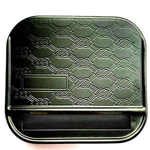 May include: A black metal rolling machine featuring a raised, embossed lattice pattern across the top surface. The device includes a rectangular recessed area on the left side and a black fabric rolling apron positioned horizontally across the centre.