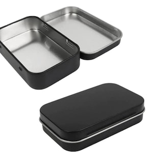 May include: A black metal tin with a hinged lid. The tin is empty and has a silver interior.