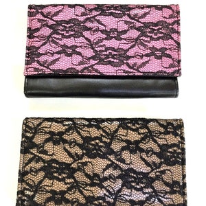 May include: Two wallets with black lace patterns on a pink and beige background. The wallets have a black leather flap.