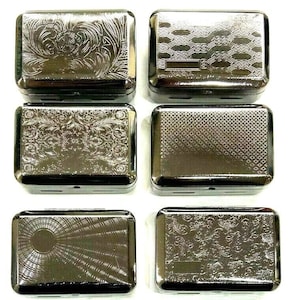 May include: Six silver metal cigarette cases with different embossed designs. The cases are rectangular and have a hinged lid.