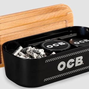May include: A black rectangular storage box with rounded corners and the OCB logo printed in white on the front. The box features a removable light wood lid and contains several small white cylindrical filters and round black OCB branded tins.