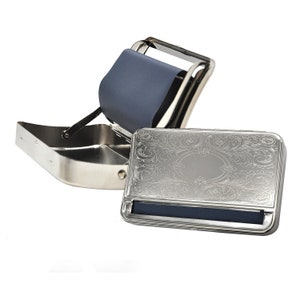 May include: A silver metal rolling tray with an engraved floral design. The tray has a built-in rolling machine with a blue plastic roller.