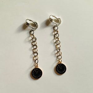 May include: A pair of gold-tone clip-on earrings with black clock face charms. The earrings have a chain link design.