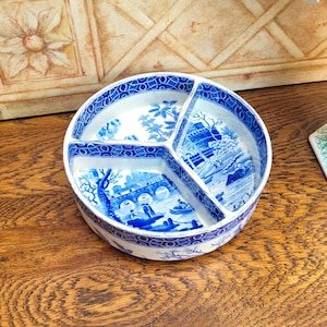 May include: A circular serving dish with three compartments, featuring a blue and white Chinoiserie pattern. Each section displays a different landscape scene. The rim and dividers are decorated. The dish is made of ceramic.