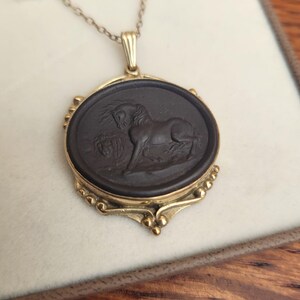 May include: Gold-toned pendant necklace featuring a dark oval cameo with a detailed relief of a horse. The pendant is framed in gold and hangs from a delicate chain. The horse is depicted in a classical style.