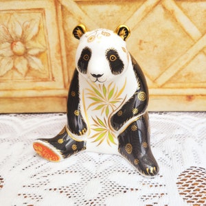 May include: A black and white porcelain panda figurine with gold accents. The panda is sitting with its legs crossed and has a bamboo design on its chest.