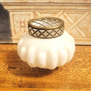 Peut inclure: Un vase en verre blanc texturé avec un crapaudine décoratif en laiton. Le vase a une forme arrondie avec une série de rainures verticales. Le crapaudine en laiton a un motif géométrique.