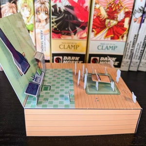 May include: A papercraft model of a room with a green tiled floor, a wooden floor, and a white countertop. The model is open and shows the interior of the room. The model is made of paper and cardboard and is painted in various colours.