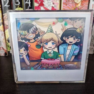 May include: A Polaroid-style photograph of four cartoon characters celebrating a birthday with a pink and white cake decorated with strawberries. The characters are wearing party hats and smiling.