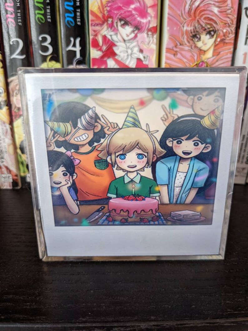 May include: A Polaroid-style photograph of four cartoon characters celebrating a birthday with a pink and white cake decorated with strawberries. The characters are wearing party hats and smiling.