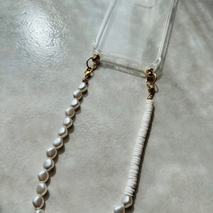 May include: A clear phone case with a white pearl and white bead phone strap.