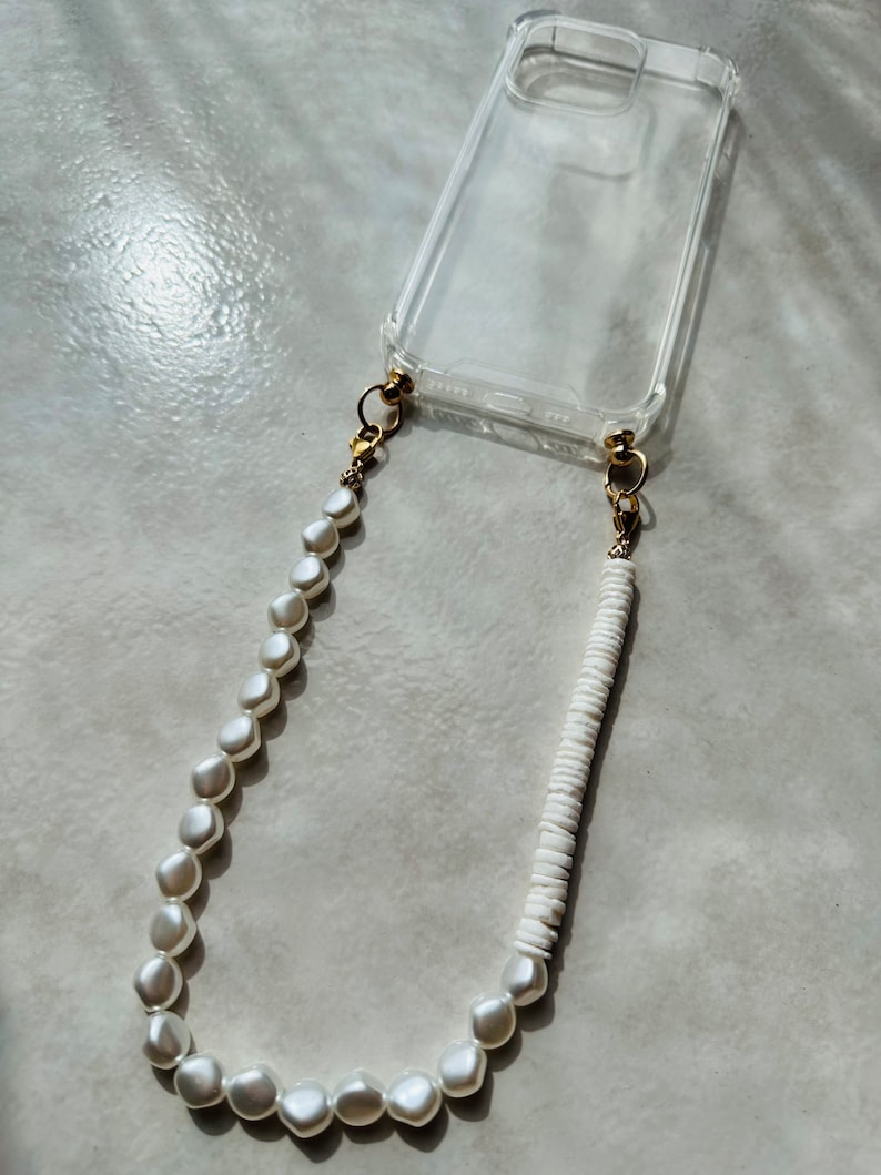 May include: A clear phone case with a white pearl and white bead phone strap.