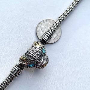 May include: A silver chain bracelet with a silver and gold panther head charm. The panther has blue gemstone eyes.