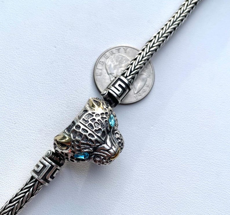 May include: A silver chain bracelet with a silver and gold panther head charm. The panther has blue gemstone eyes.