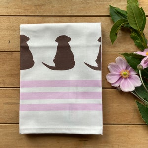 May include: A white kitchen towel with pink stripes and a brown silhouette of three dogs printed on it.