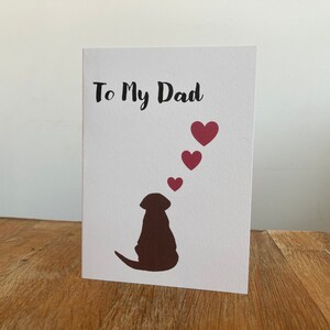 Pode incluir: Um cart&atilde;o branco com o texto "To My Dad" em letras pretas. Uma silhueta marrom de um cachorro est&aacute; na parte inferior do cart&atilde;o, com cinco cora&ccedil;&otilde;es rosa flutuando acima da cabe&ccedil;a do cachorro.