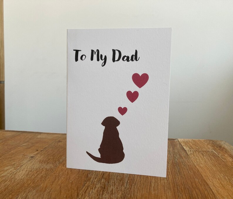 Pode incluir: Um cart&atilde;o branco com o texto "To My Dad" em letras pretas. Uma silhueta marrom de um cachorro est&aacute; na parte inferior do cart&atilde;o, com cinco cora&ccedil;&otilde;es rosa flutuando acima da cabe&ccedil;a do cachorro.