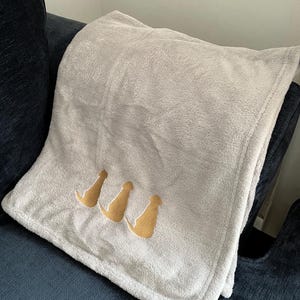 May include: A soft, gray fleece throw blanket with three gold dog silhouettes embroidered on it.