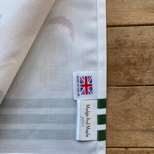 Pode incluir: Close-up de um tecido listrado branco e verde com uma etiqueta que diz "Madge And Maple" e "MADE IN THE UK" com uma bandeira Union Jack. O tecido tem um padr&atilde;o de formas vermelhas.