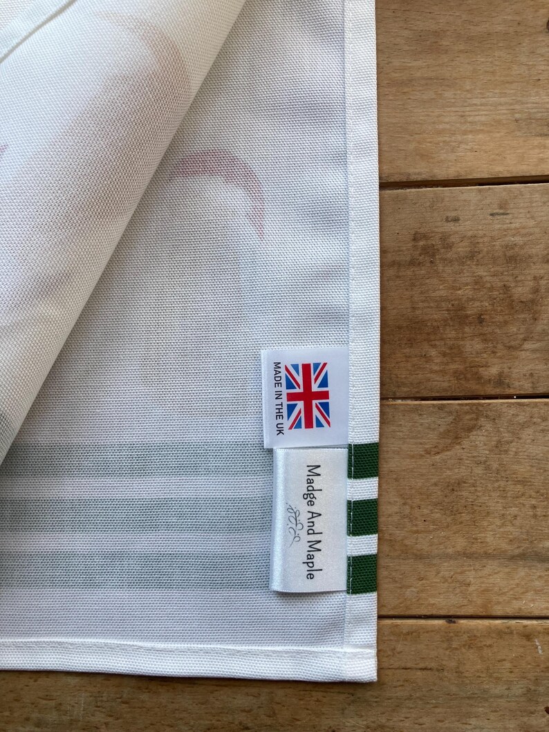 Pode incluir: Close-up de um tecido listrado branco e verde com uma etiqueta que diz "Madge And Maple" e "MADE IN THE UK" com uma bandeira Union Jack. O tecido tem um padr&atilde;o de formas vermelhas.