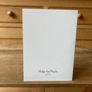 Pode incluir: Um cart&atilde;o branco em branco com o texto "Madge And Maple" impresso em preto na parte inferior.